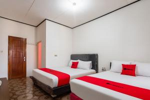 two beds in a room with red and white at RedDoorz near Pantai Ujung Genteng 2 in Ujunggenteng