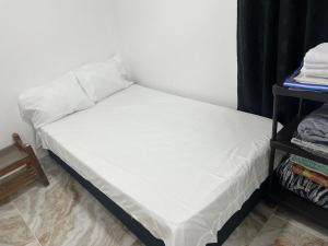 una cama con sábanas blancas en una habitación en Casa Linda, en Armenia