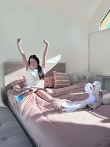 Una niña sentada en una cama con los brazos en el aire. en ณิชาวิลล่า ริเวอร์ฟร้อนท์ บ้านท่าตอน Nicha Villa Riverfront BanThaton, en Mae Ai Chiang Mai