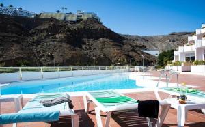 una piscina con sillas, una mesa y una montaña en Peñamar Tour, en Puerto Rico de Gran Canaria