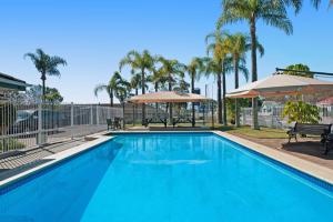 una gran piscina azul con bancos y sombrillas en Colonial Terrace Motor Inn en Raymond Terrace