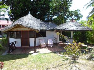 a small hut with a thatched roof and two chairs at Amitie Chalets Praslin in Grand Anse