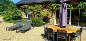 a wooden table with chairs and an umbrella at La Forcerie maison d'hôtes et spa in Châtelais