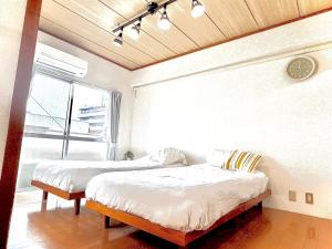 two beds in a room with a clock on the wall at Kumamoto Serviced Apartment Sakura Mee 桜美 in Kumamoto