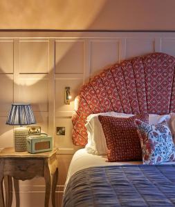 uma cama com uma cabeceira vermelha e uma mesa com um candeeiro em The Potters Heron - A Heartwood Inn em Romsey