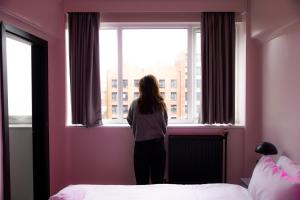 a woman standing in a bedroom looking out the window at Malacuna Liverpool in Liverpool