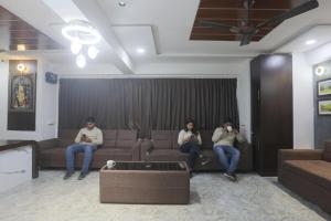 three people sitting on a couch in a living room at Hotel Brook View in Surat