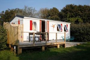 a small white house with a wooden deck at Mobil-home Les volets rouges in Plouhinec