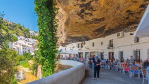 a crowd of people sitting outside a restaurant under a cliff at Cueva El Arrabal Setenil by Ruralidays in Setenil