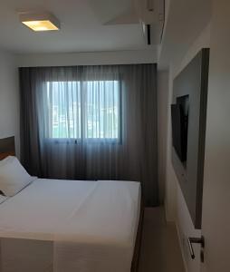 Un dormitorio con una cama blanca y una ventana. en Arte Studios - Flats decorados, wifi, estacionamento, piscina, academia, en Río de Janeiro