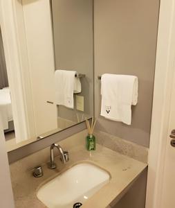Un baño con lavabo, espejo y toallas. en Arte Studios - Flats decorados, wifi, estacionamento, piscina, academia, en Río de Janeiro