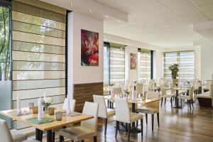 Un comedor con mesas y sillas blancas. en NH Oberhausen, en Oberhausen
