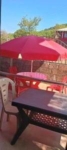 uma mesa de piquenique com um guarda-chuva vermelho no pátio em Junglee Valley Holiday Home em Mahabaleshwar