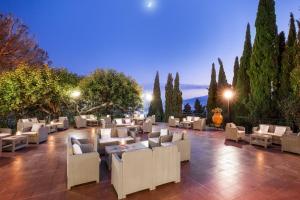 タオルミーナにあるヴィラ ディオドロ ホテルの白い椅子とテーブル、木々が並ぶパティオ