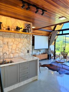 a kitchen with a stone wall and a tv at Dalbérgia Chalés - Mantiqueira MG in Gonçalves