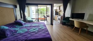 a bedroom with a purple bed with a desk and a kitchen at Fare Tupaia in Arue