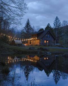 a log cabin at night with a reflection in the water at Boutique Log Cabin & Two Guest Cabins, Hot Tub, Sauna, Swimming Hole, near Whiteface in Upper Jay