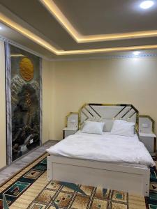 a bedroom with a white bed with a painting on the wall at Хостел Истиклол in Fergana