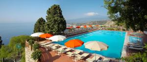 een groot zwembad met parasols en stoelen bij Hotel Villa Diodoro in Taormina