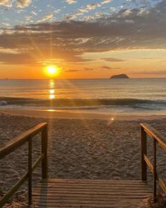 a sunset on a beach with a wooden pier at HosteldaRo in Penha