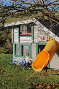 Tongariro Cottage - Hot Tub - Bring Your Dog! في Raurimu: فتاة صغيرة تلعب على زلاجة أمام منزل +30 صورة