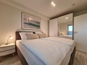 ein Schlafzimmer mit einem großen weißen Bett und einem Spiegel in der Unterkunft Meeresblick Pier 23 H2 WE 23 in Hohwacht