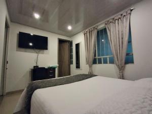 um quarto com uma cama branca e uma TV de tela plana em C habitación con baño privado em Bogotá