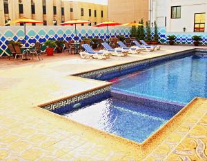 einen Pool mit Stühlen, Tischen und Sonnenschirmen in der Unterkunft Bahrain International Hotel in Manama