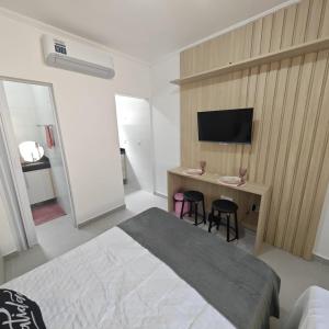 a bedroom with a bed and a desk with a television at Apartamento no Centro de Mongaguá, perto da praia! in Mongaguá