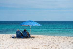 LafitteCasa Palma - 2BR - Pool Palms & Paradise的两人坐在海滩上一把遮阳伞下的椅子上