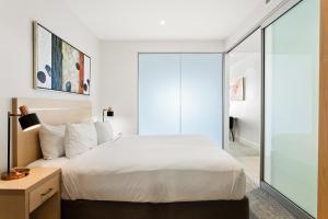 a bedroom with a white bed and a glass wall at Belle Escapes - Waves at The Bay in Glenelg