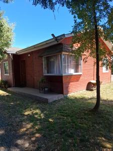a small red house with a porch and a tree at Cabañas San Sebastián 2 in Angachilla