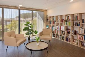 a library with two chairs and a table and bookshelves at Quality Suites Saint-Paul-l s-Dax in Saint-Paul-lès-Dax
