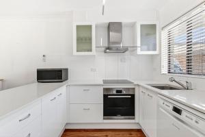 Surf's Up Sawtell في ساوتيل: مطبخ أبيض مع دواليب بيضاء ومغسلة +4 صور