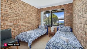 a room with two beds and a chair and a window at Cuttagee Beach Cottage 3 - Tathra Bermagui Rd 3521 in Barragga Bay