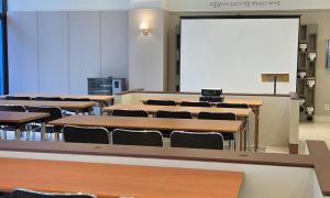 uma sala de aula com mesas e cadeiras e um ecrã branco em Firstcity Hotel YEOSU em Yeosu