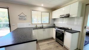a kitchen with white cabinets and a black counter top at Tanjil Cottage in Lakes Entrance