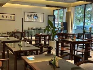 Un restaurante con mesas y sillas de madera y ventanas. en Serene Peaks Courtyard-Free pick-up-Free Laundry, en Fenghuang