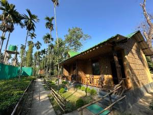 a wooden house with a porch and palm trees at Kaziranga Tea Nest Homestay in Kāziranga