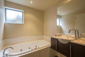 a bathroom with a tub and a sink and a mirror at LakeRidge Queenstown by Staysouth in Queenstown +15 photos