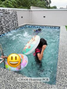 a little girl in a swimming pool with a surfboard at CHAM Homestay PCB in Kota Bharu