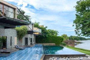 a house with a swimming pool next to a river at The Xcape River Kwai in Kanchanaburi