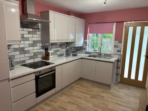 a kitchen with white cabinets and pink walls at Birch View, Woodhall Spa in Woodhall Spa