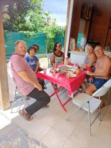 eine Gruppe von Menschen sitzt um einen roten Tisch in der Unterkunft Bungalow charmant à Château Gaillard avec piscine partagée in Le Moule