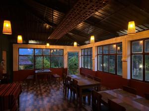 um restaurante com mesas e cadeiras de madeira e janelas em Aruvi Mountain Villa Vagamon by VOYE HOMES em Vagamon