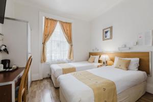 a bedroom with two beds and a desk and a window at Falcon Hotel in London