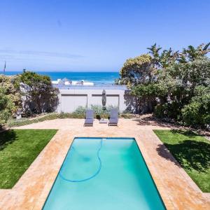 een zwembad met twee stoelen en de oceaan op de achtergrond bij BB BEACH BAY QUALITY APARTMENTs in Cape Town