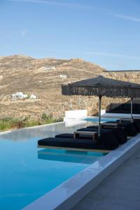 a swimming pool with lounge chairs and an umbrella at Aora Villa Ftelia Beach Mykonos in Panormos Mykonos