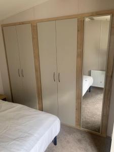 Schlafzimmer mit weißen Schränken, einem Bett und einem Spiegel in der Unterkunft Lovely 6 Berth Caravan With Free Wi-Fi At Harts Holiday Park, Kent Ref 74068W in Leysdown-on-Sea + 4 Fotos