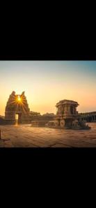 a sunset in a desert with a building in the foreground at Puneetha home stay hampi in Hampi